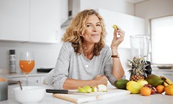 Woman smiling while snacking on fruit in kitchen