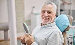 
A happy elderly man sitting in a dental chair and holding a hand mirror